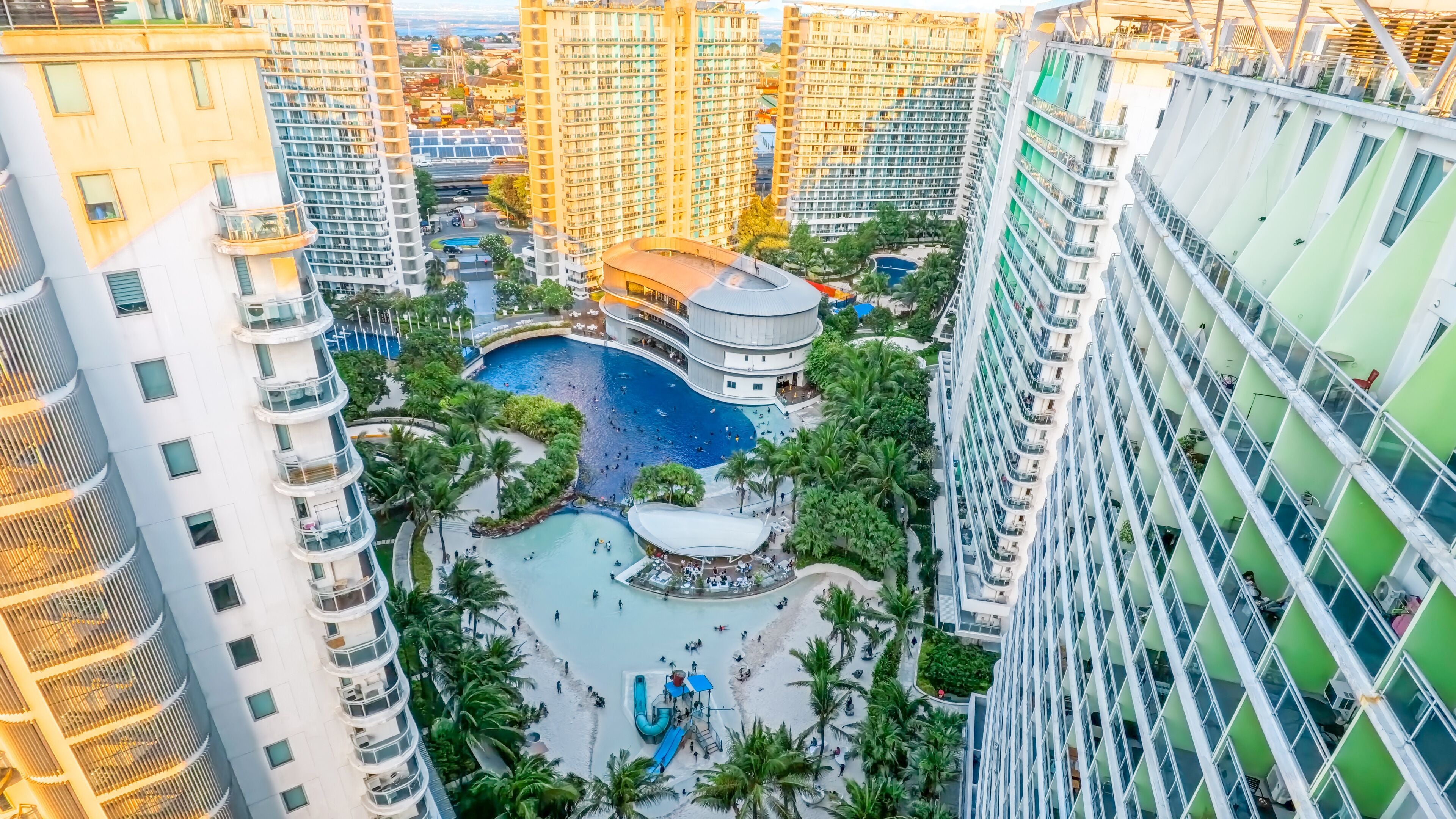 Un edificio de gran altura con un patio central que cuenta con una piscina, rodeado de exuberante vegetación y palmeras.