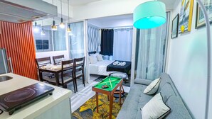 A compact hotel room with a dining area, a bed with a black headboard, a sofa, a pool table, and a large window with curtains. - Stunning 1-bed Apartment in Paranaque (Parañaque)