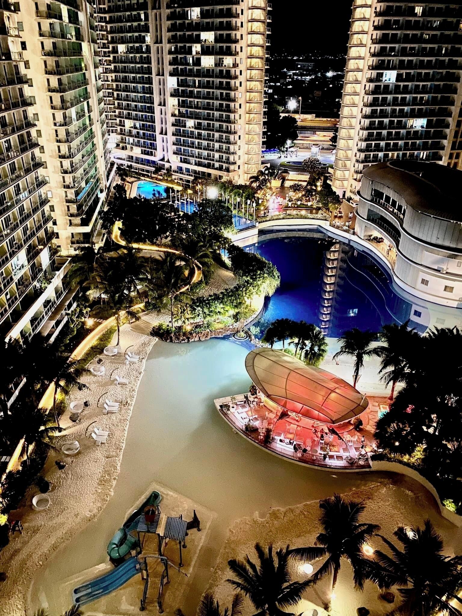 Un hotel moderno de gran altura con múltiples balcones, una piscina central y una zona de juegos para niños.