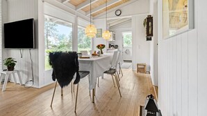 Een eetruimte met een witte tafel, stoelen en een aan de muur bevestigde televisie.