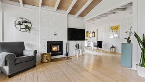 Een moderne woonkamer met een open haard, een bank, een televisie en een eethoek met stoelen en een tafel.