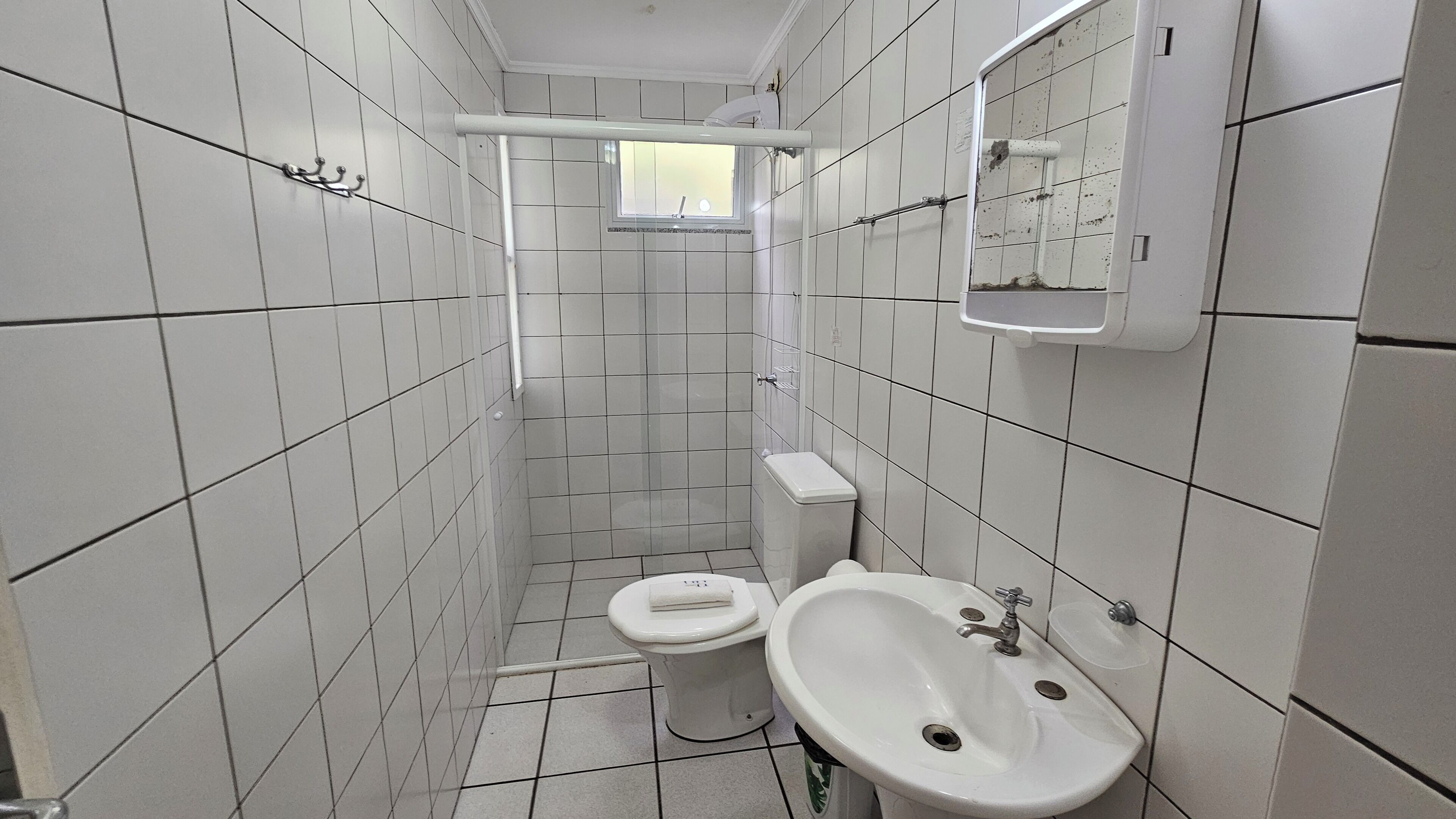 Une petite salle de bain carrelée, équipée de toilettes, d’un lavabo et d’une fenêtre.