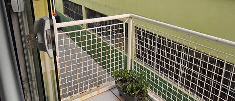 Un balcón con barandilla metálica, una planta en maceta y vistas de edificios vecinos.