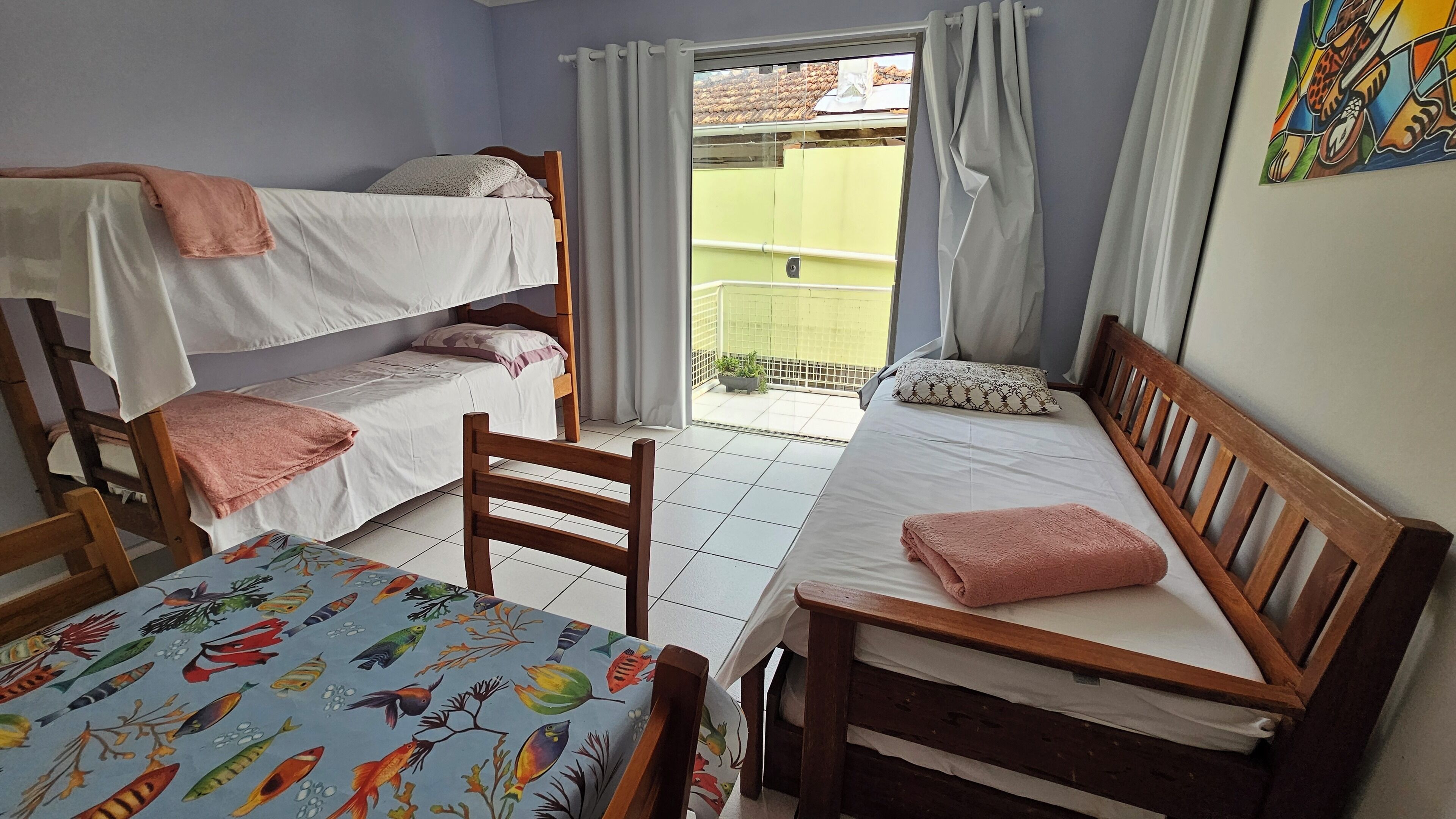 A dormitory room with bunk beds, a single bed, and a table with a colorful tablecloth.