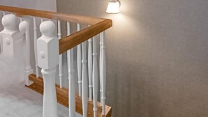 Eine Holztreppe mit weißen Geländern und einer an der Wand befestigten Leuchte.