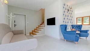 Ein modernes Wohnzimmer mit Treppe, Sofa, blauem Sessel und Wand-Fernseher.