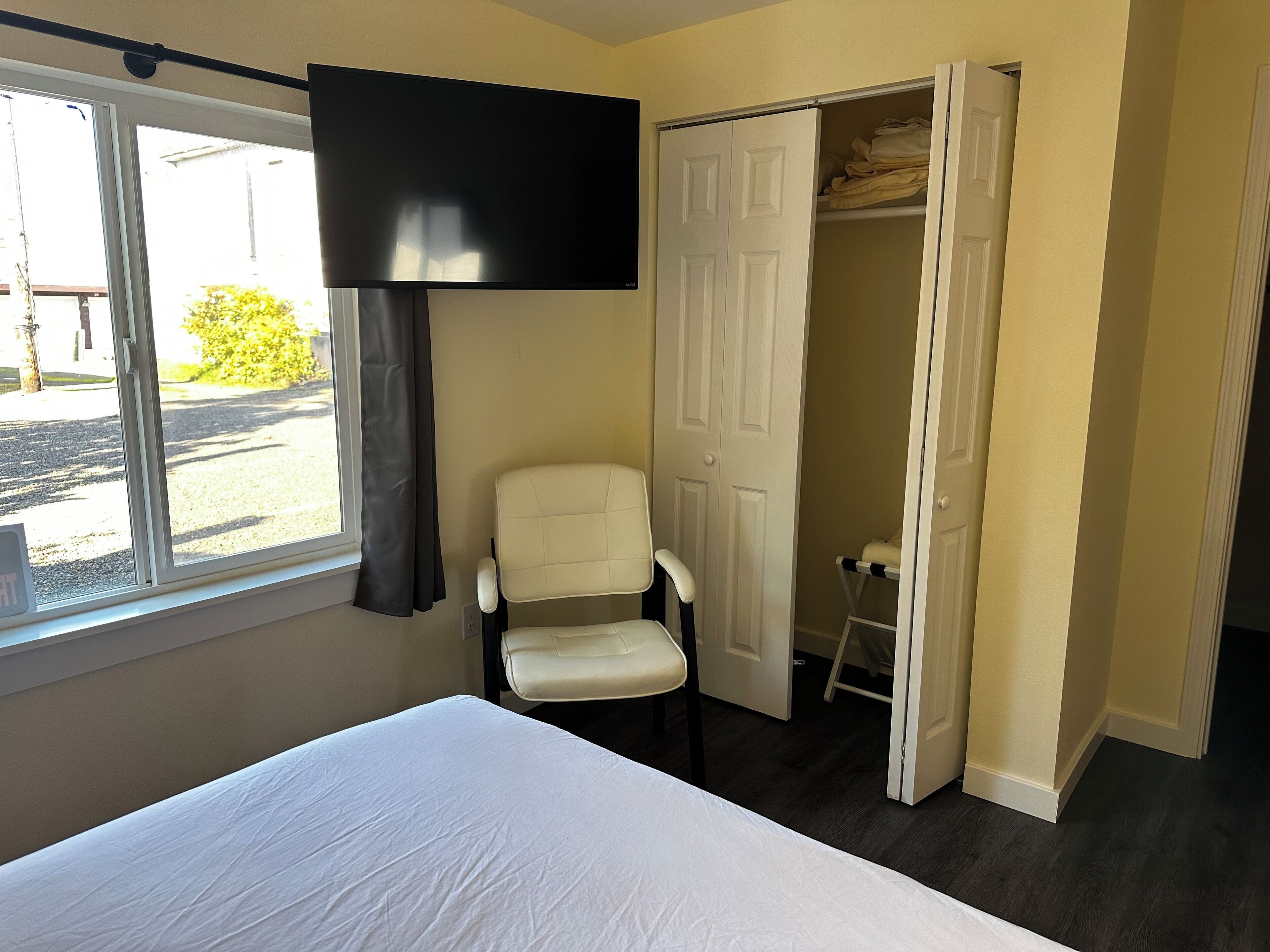 A hotel room with a bed, a chair, a TV, and a wardrobe.