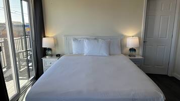 A hotel room with a large bed, two bedside tables with lamps, a white headboard, and a view through a sliding door to the outside.