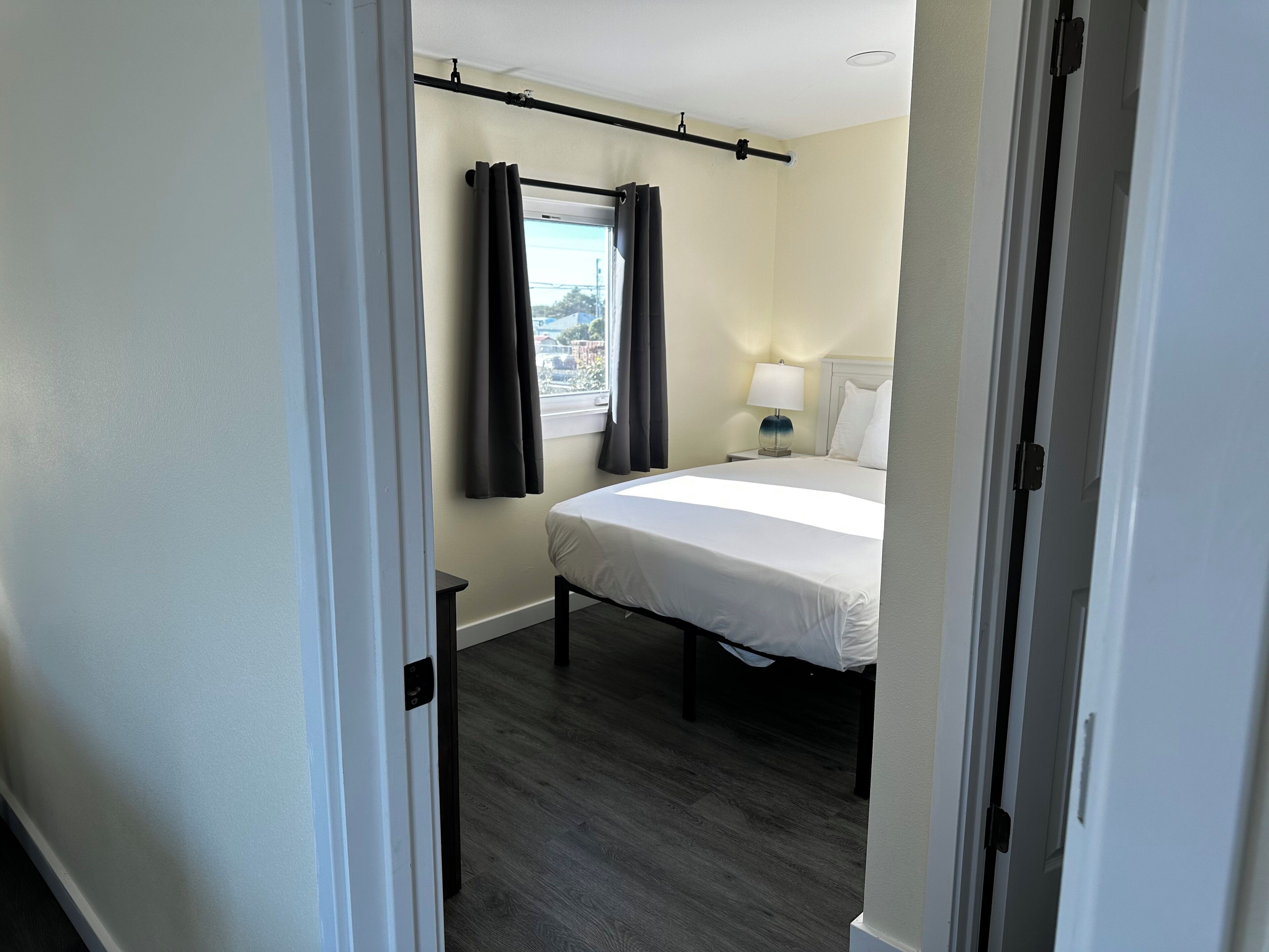 A hotel room with a bed, a nightstand, a lamp, and a window with curtains.