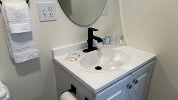 A bathroom with a white sink, black faucet, and a mirror above it. There are toiletries on the sink and a towel rack with a white towel.