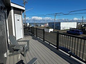 A wooden deck with a bench and a small table, overlooking a street with a blue car and a stop sign. - Dock Street Inn (Westport)