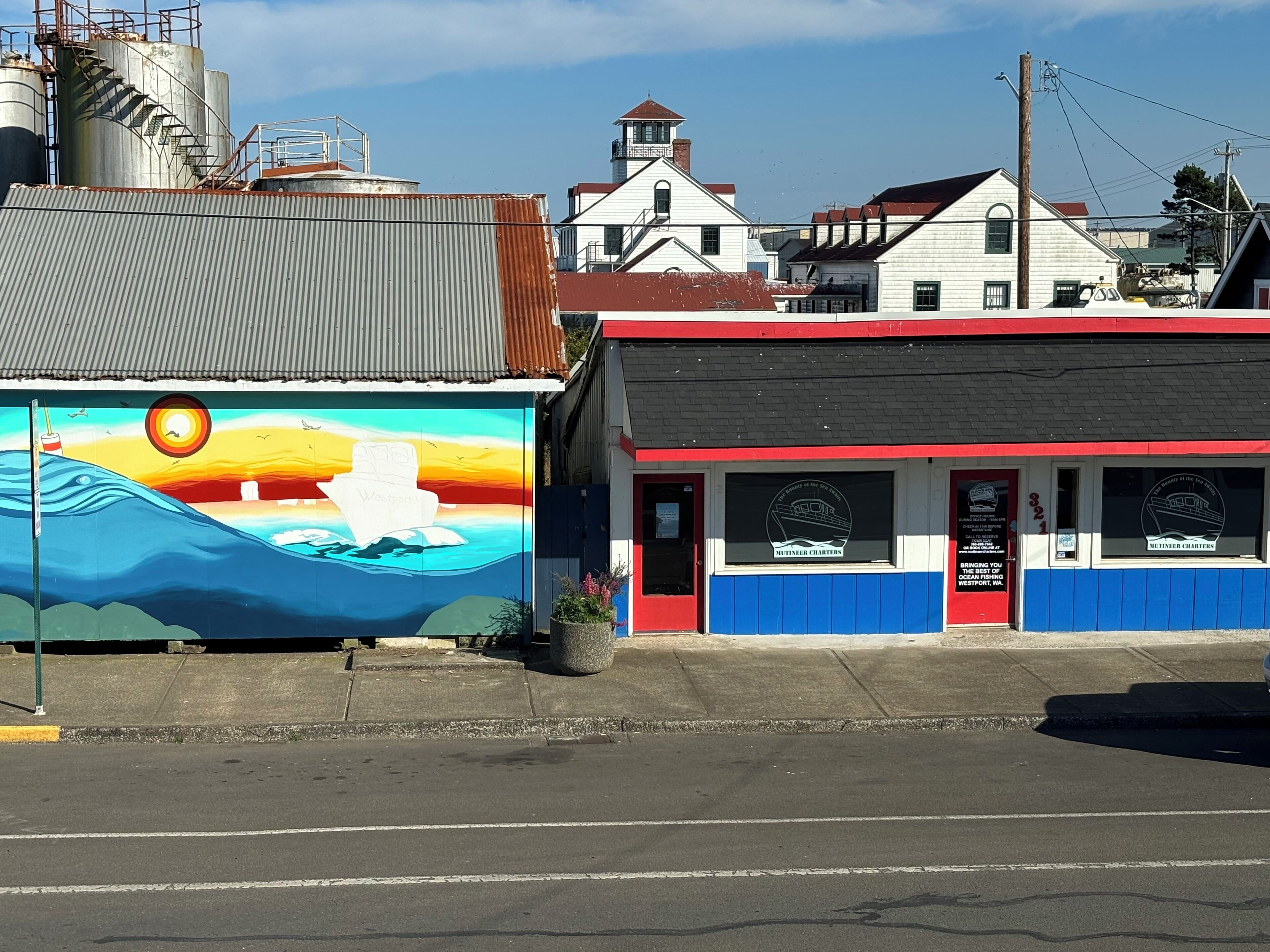 A building with a mural of a sunset over water, a red and white facade, and a sign for 'MUTINER CHARTERS'.