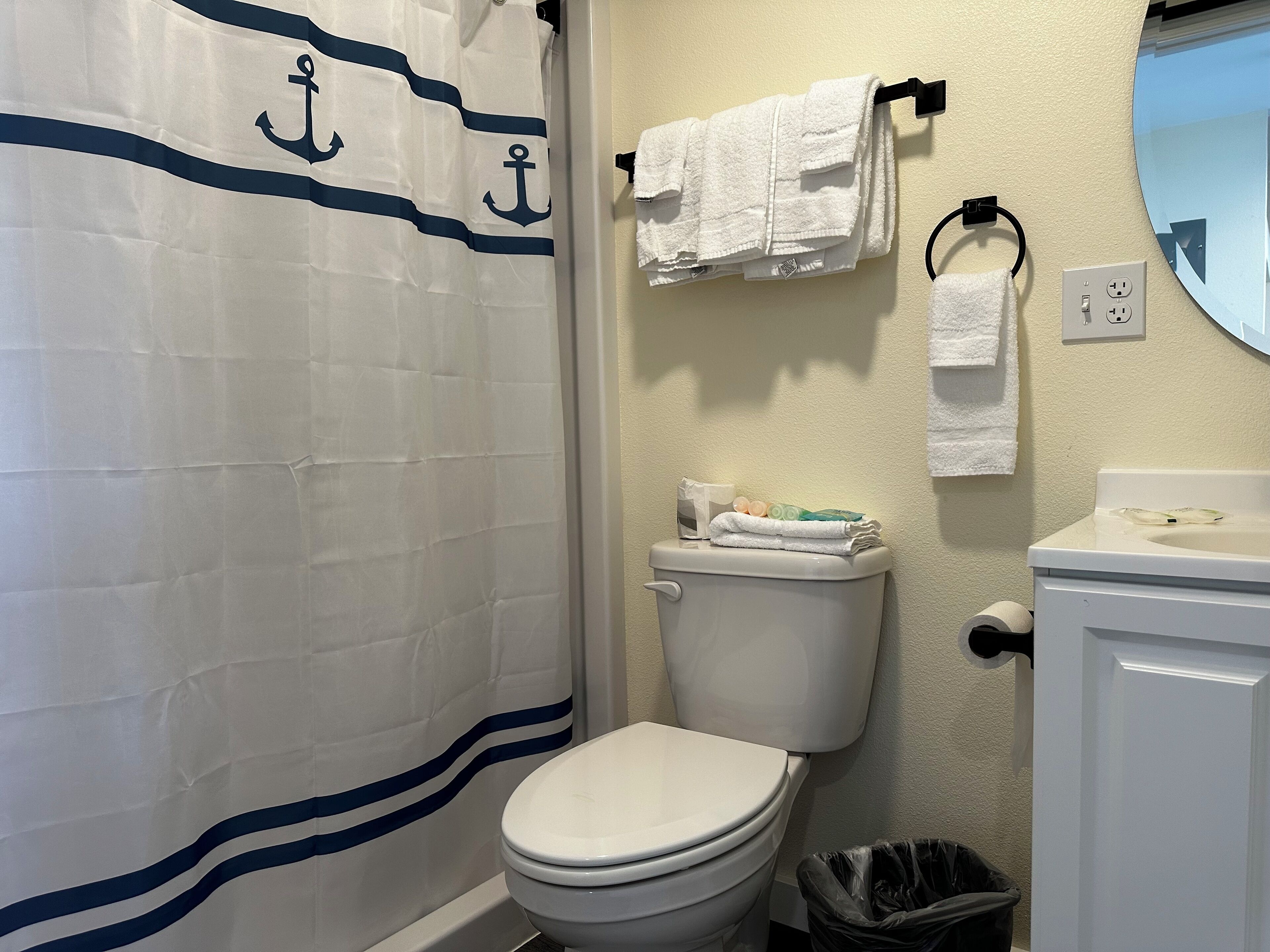 Un baño con inodoro, lavabo, espejo y cortina de ducha con motivos de anclas.