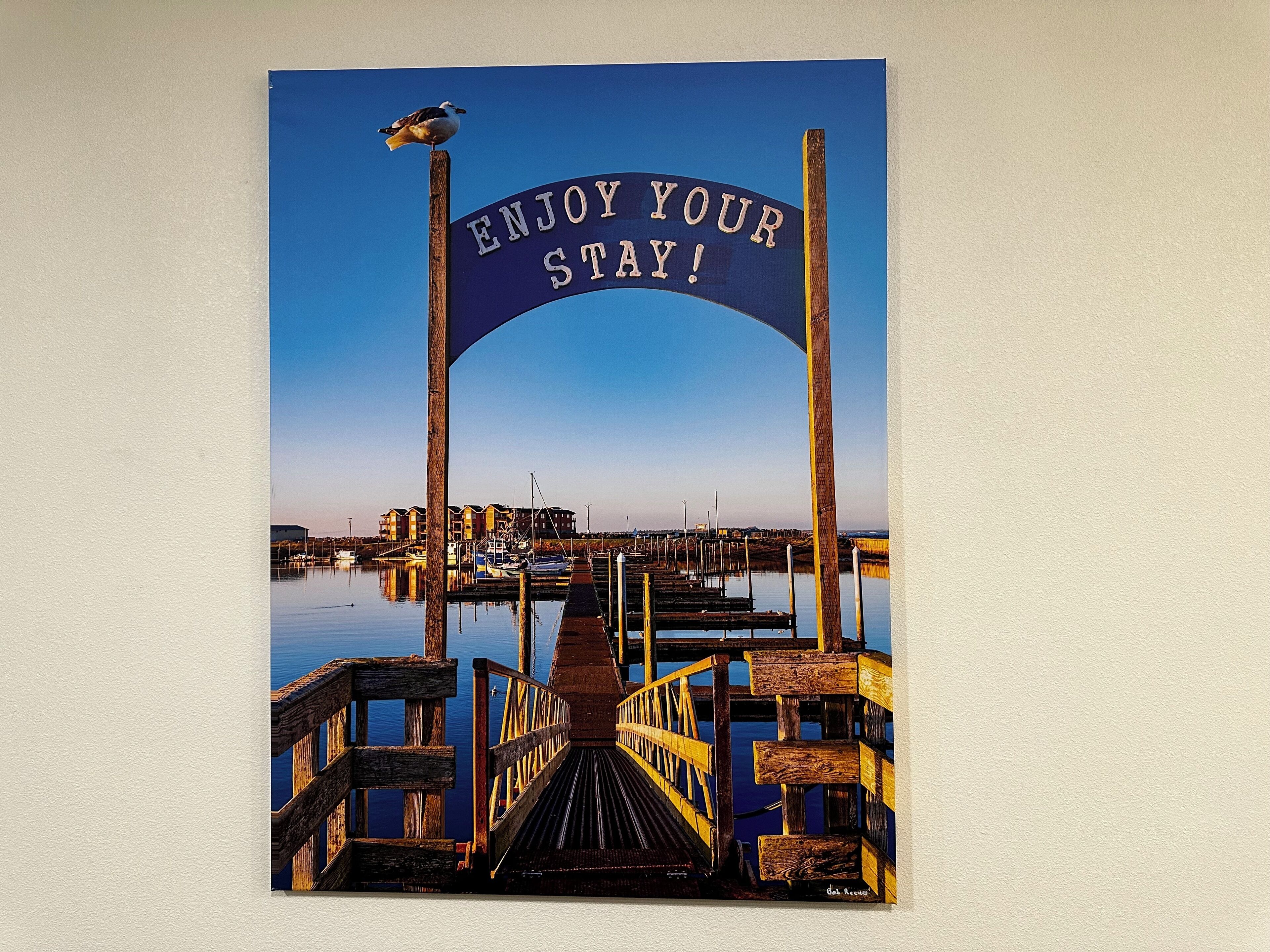 A wooden pier leading to a dock with a sign that reads "ENJOY YOUR STAY!"