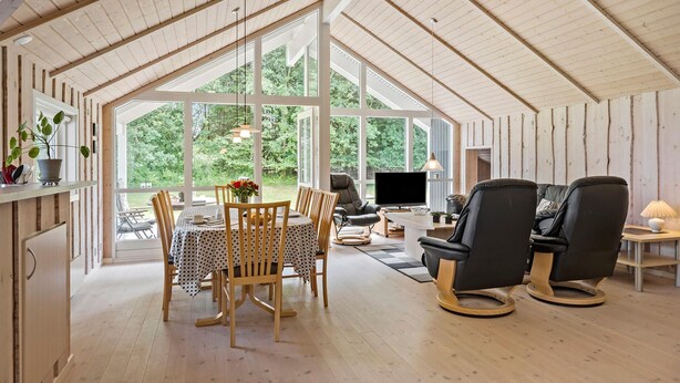 Une pièce spacieuse avec un plafond haut et de grandes fenêtres, un coin repas avec une table et des chaises, un canapé et un téléviseur.