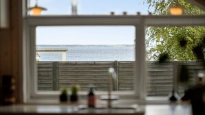 Une vue depuis une fenêtre ornée d’un garde-corps en bois, donnant sur une étendue d’eau et une côte lointaine.