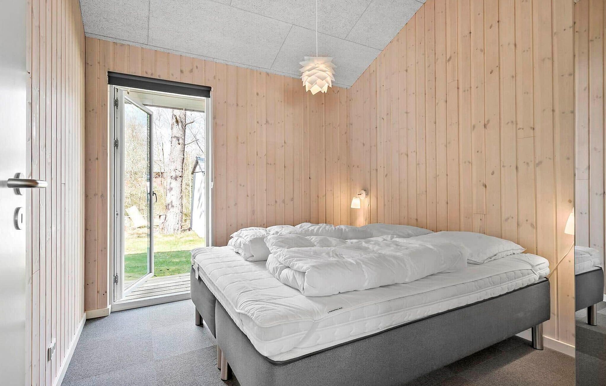 Une chambre à coucher avec un lit, une porte donnant sur l’extérieur et un luminaire fixé au mur.