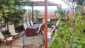 An outdoor patio with a wooden table and chairs, surrounded by a metal fence and greenery. - Lovely apartment in Trabia with house sea view (Trabia)