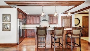 A spacious kitchen with wooden cabinets, a central island with bar stools, pendant lighting, and a stainless steel refrigerator. - Vail Ritz Carlton 3 Bedroom Residence (Vail)