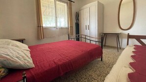 A bedroom with a bed, a wardrobe, a mirror, and a window with curtains. - Maison de 2 Chambres Pour 4 Personnes (Marseillan)