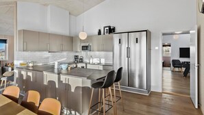 Una cocina moderna con una isla central, electrodomésticos de acero inoxidable y un comedor con taburetes de bar.