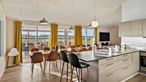 Una cocina moderna con una isla grande, comedor con sillas y vistas amplias a través de grandes ventanales.