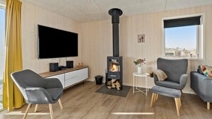 Una sala de estar moderna con un televisor de pantalla plana grande, un hogar de leña negro, sillones grises y un mueble de madera.