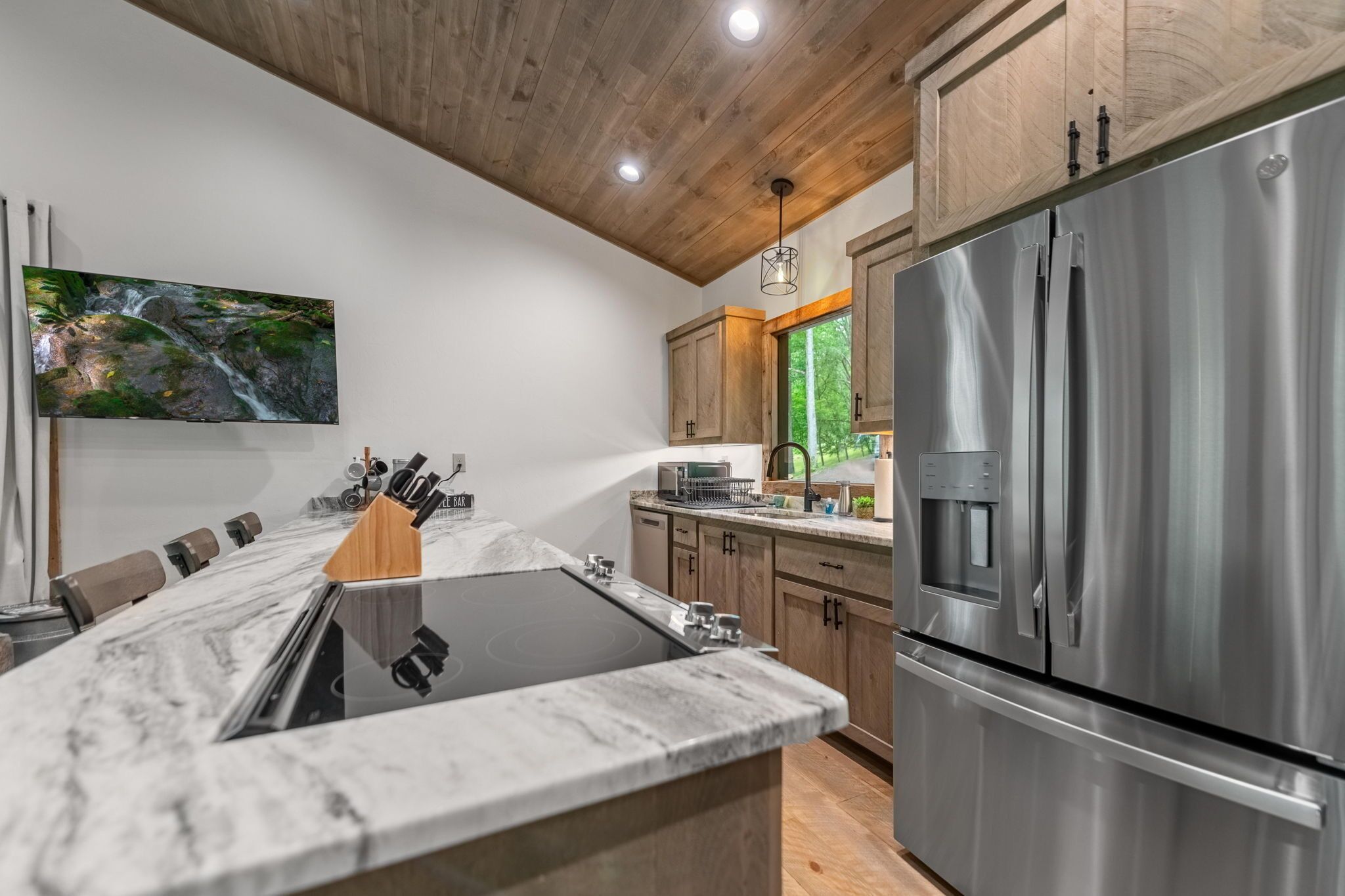 Una cucina moderna con un'isola grande, elettrodomestici in acciaio inossidabile, mobili in legno e un grande televisore montato a parete.