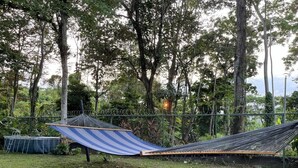 A hammock set up in a grassy area with a metal fence and trees in the background. - Hotel Azul Coral (Cahuita)