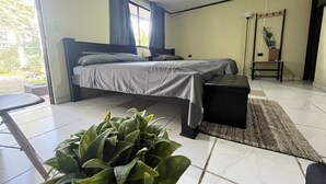 A bedroom with two beds, a bench, a potted plant, and a window with curtains. - Hotel Azul Coral (Cahuita)
