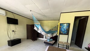A room with a bed, a hammock, a TV, a cabinet, and a painting. - Hotel Azul Coral (Cahuita)