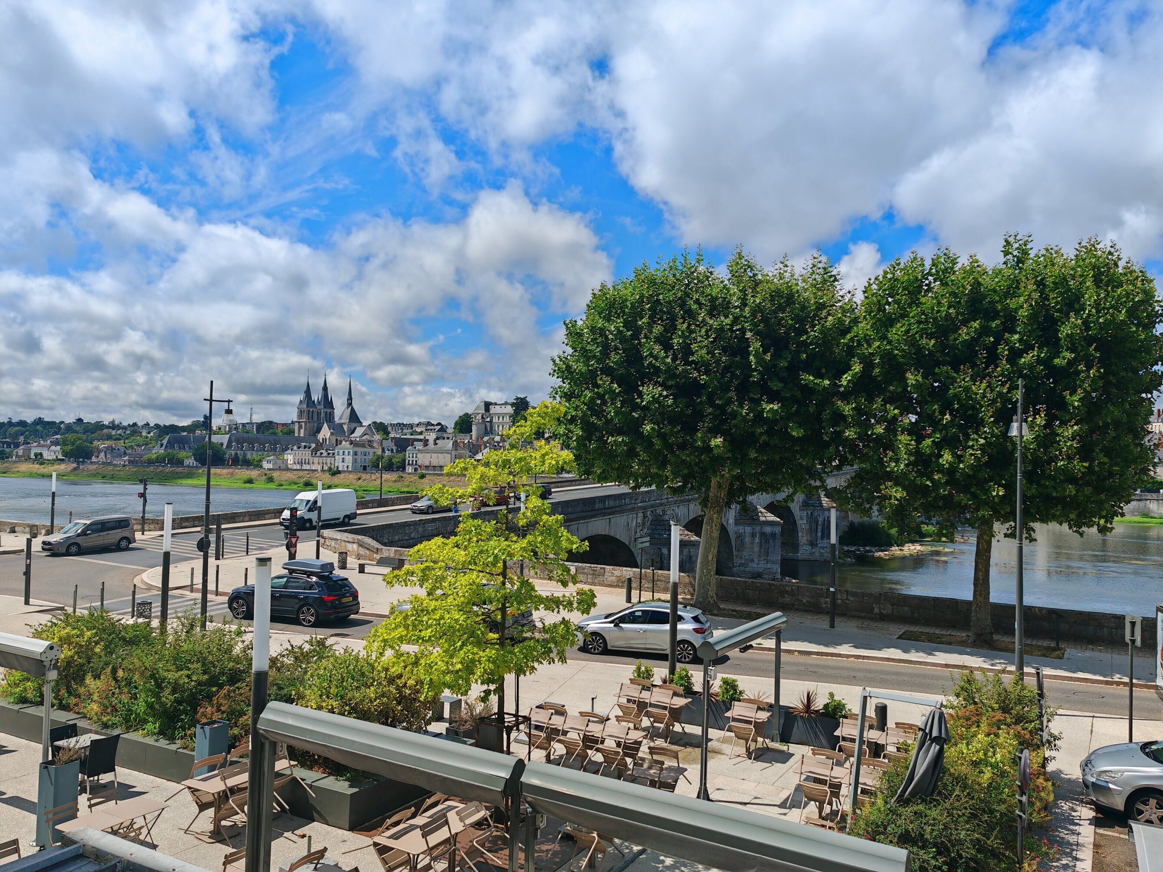 Une vue sur la rivière, avec un pont, des arbres et un bâtiment historique en arrière-plan.