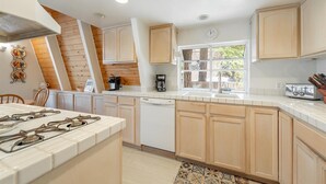 Une cuisine avec des meubles en bois, une cuisinière, une machine à café et une fenêtre donnant sur les arbres.
