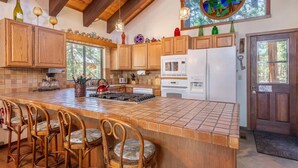 A kitchen with wooden cabinets, a large island with bar stools, a microwave, and a refrigerator. - Viani Cabin (Carnelian Bay)