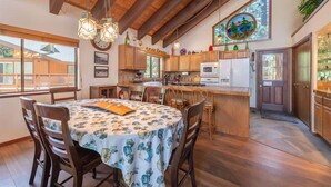 A kitchen with wooden beams, a dining table with chairs, and a view of the outside. - Viani Cabin (Carnelian Bay)