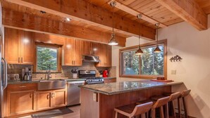 Una cocina moderna con armarios de madera, una isla central con taburetes de bar, electrodomésticos de acero inoxidable y un amplio ventanal con vistas al exterior.