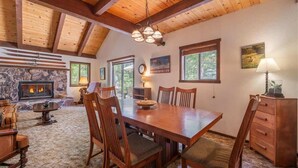 A spacious dining area with a large wooden table and chairs, a stone fireplace, and a high wooden ceiling.