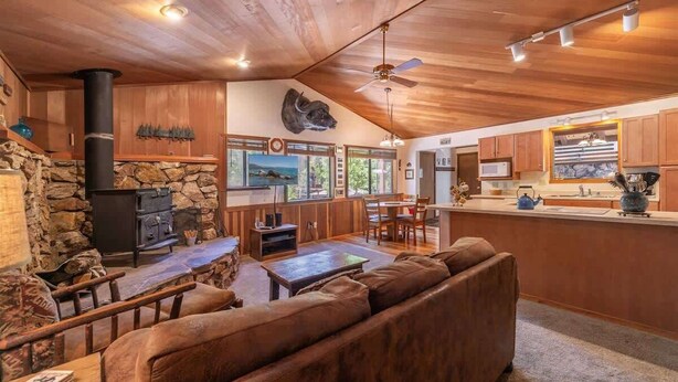 A rustic cabin interior with a stone fireplace, wooden ceiling, and a cozy seating area.