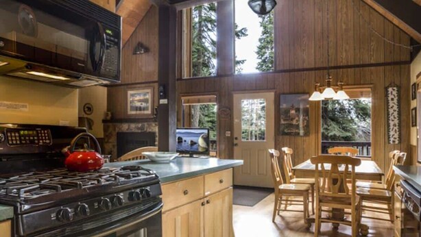 A kitchen with wooden cabinets, a stove, and a dining area with wooden chairs.