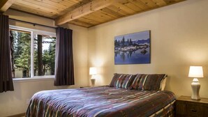 Ein Schlafzimmer mit Holzboden, einem großen Bett mit gestreifter Bettwäsche, einem Gemälde eines Sees und zwei Nachttischlampen.