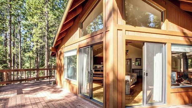 A wooden cabin with large sliding glass doors, a deck, and a forest backdrop. - Yemoto Cabin (Carnelian Bay)