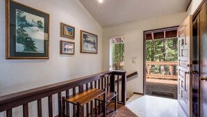 A hallway with a wooden bench, framed artwork on the walls, and a door leading to an outdoor area. - Yemoto Cabin (Carnelian Bay)