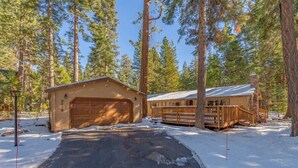 A cabin with a garage and a deck, surrounded by tall pine trees and snow on the ground. - Zoss Cabin (Carnelian Bay)