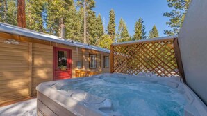 A wooden cabin with a hot tub in the foreground, surrounded by a wooden deck and a lattice fence. - Zoss Cabin (Carnelian Bay)