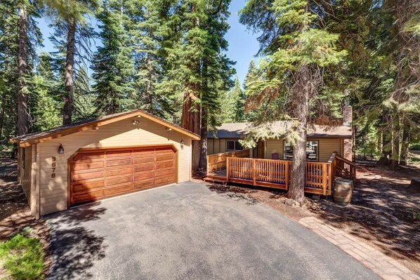 A two-story cabin with a garage and a deck, surrounded by tall pine trees. - Zoss Cabin (Carnelian Bay)