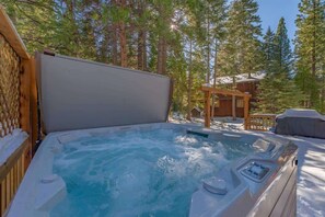 A hot tub surrounded by a wooden deck and snow, with a wooden cabin in the background. - Zoss Cabin (Carnelian Bay)