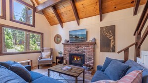 A cozy living room with a fireplace, a comfortable sofa, and a view of the outdoors. - Agate Bay Pines (Carnelian Bay)