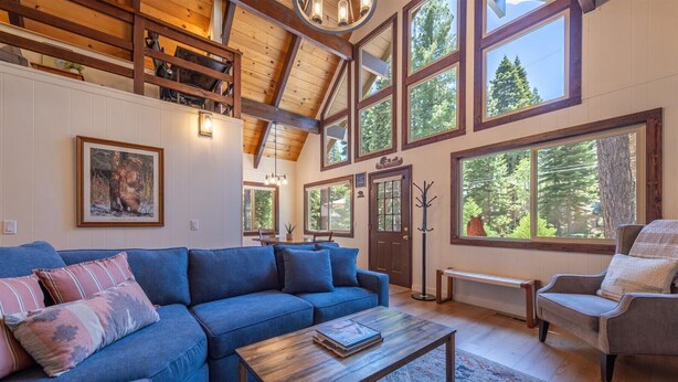 A spacious living room with a blue sofa, a wooden coffee table, and a large window overlooking a forest. - Agate Bay Pines (Carnelian Bay)