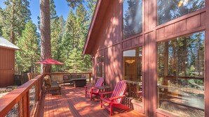Una terraza de madera con mobiliario exterior, ventanas amplias y vista a un bosque.