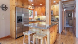 Una cocina con armarios de madera, un refrigerador de acero inoxidable, una encimera de granito y una ventana con vista a una terraza.